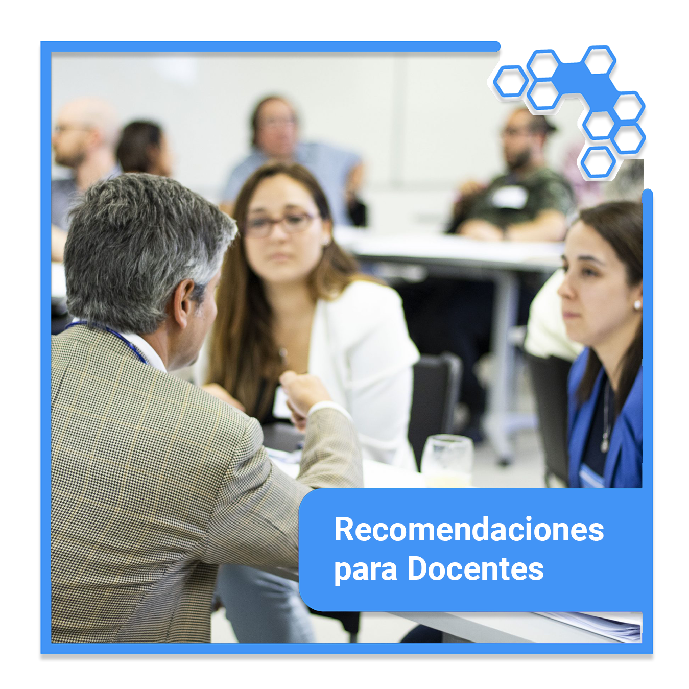 Docentes sentados conversando en una sala con otros docentes de fondo